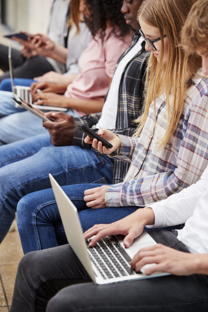 a row of teenagers using different technologies.