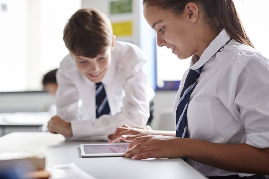 Two High School Students Wearing Uniform Working Together At Desk Using Digital Tablet