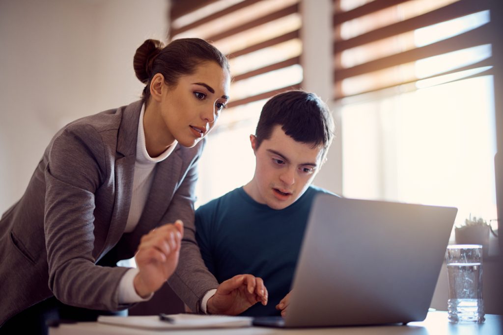 Special education teacher and man with down syndrome using laptop together.